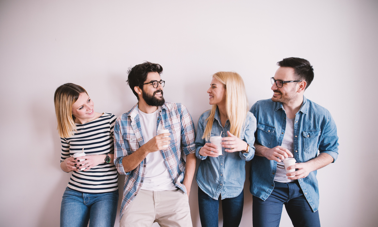 Group-of-young-stylish-happy-people-leaning-against-the-wall-and-talking-while-drinks-coffee-in-the-paper-cup.-944868364_1323x796